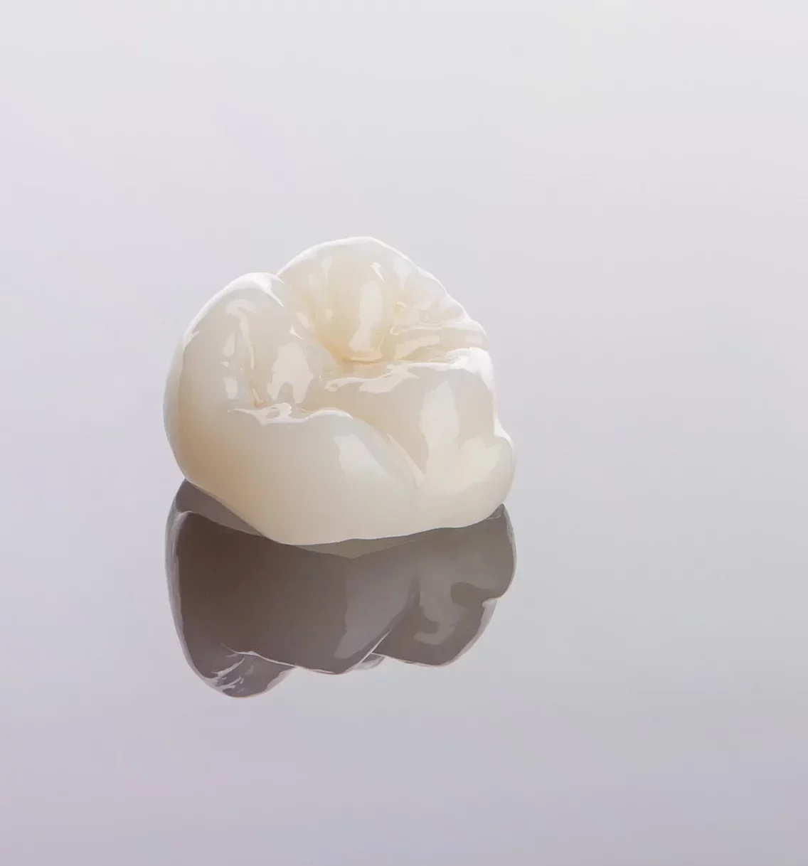 Pojedyncza porcelanowa korona zębowa na lustrzanej powierzchni – nowoczesna rekonstrukcja protetyczna